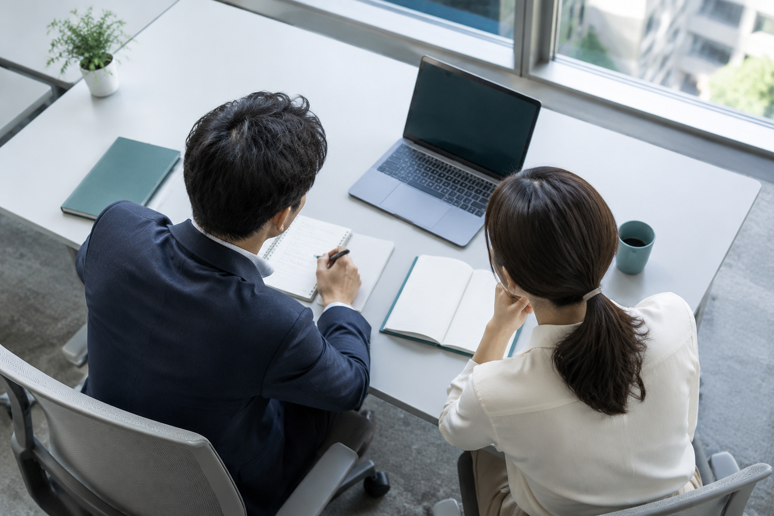 Two colleagues talking across an office table, seen from behind