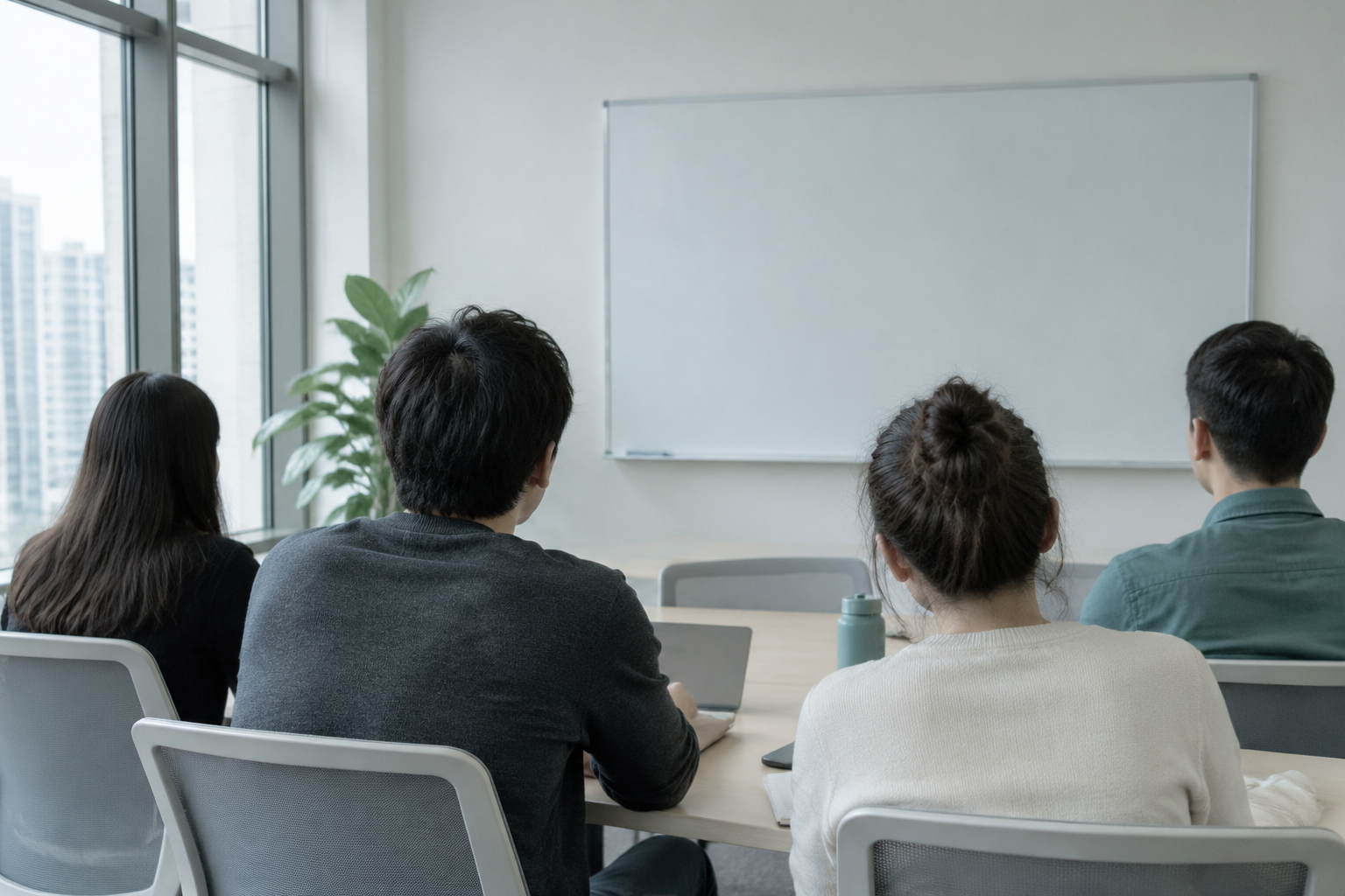 Four people around a meeting table seen from behind, blank whiteboard ahead